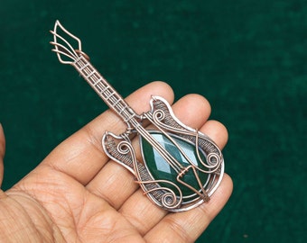 May include: A copper wire guitar pendant featuring a green gemstone at its centre. The pendant is intricately detailed and has a wire-wrapped design.