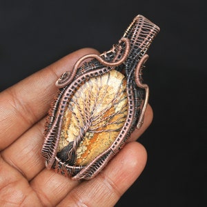 May include: A copper wire wrapped pendant featuring a tree agate stone with a brown and white pattern. The pendant is oval shaped and has a copper wire loop at the top for hanging.