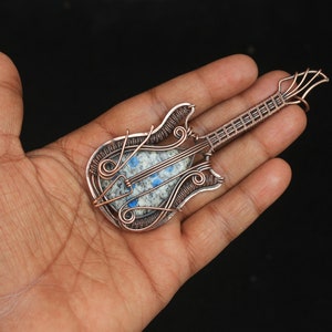 May include: A copper wire wrapped guitar pendant with a blue and white stone in the center.