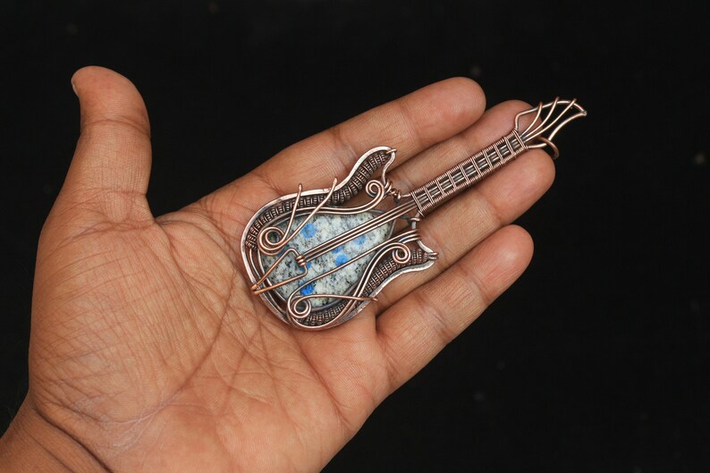 May include: A copper wire wrapped guitar pendant with a blue and white stone in the center.