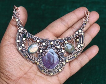 May include: A copper wire wrapped necklace with a large amethyst gemstone and two smaller labradorite gemstones. The necklace is decorated with small gold beads.