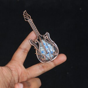 May include: A copper wire wrapped guitar pendant with a blue and white stone inlay.