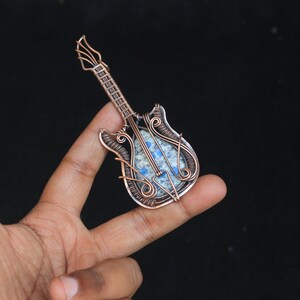 May include: A copper wire wrapped guitar pendant with a blue and white stone in the center.