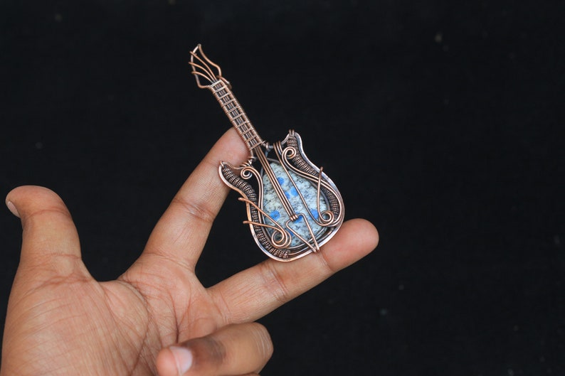 May include: A copper wire wrapped guitar pendant with a blue and white stone in the center.