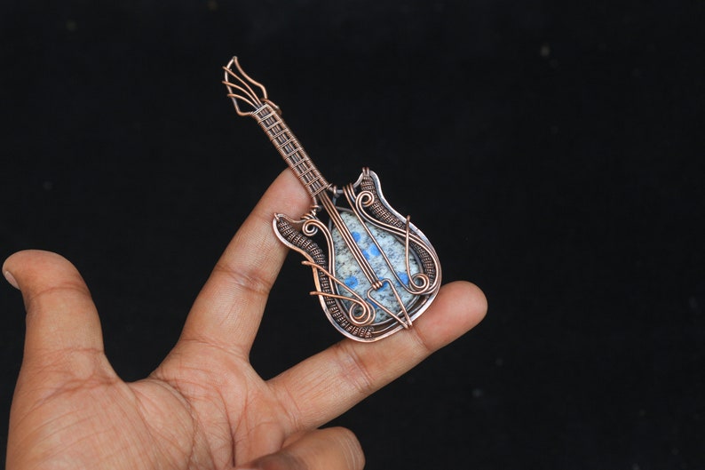 May include: A copper wire wrapped guitar pendant with a blue and white stone inlay.