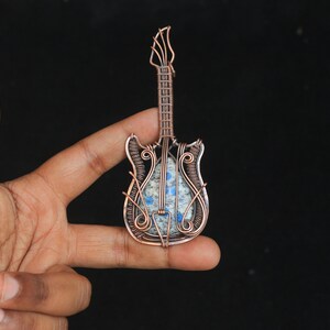 May include: A copper wire wrapped guitar pendant with a blue and white stone inlay.