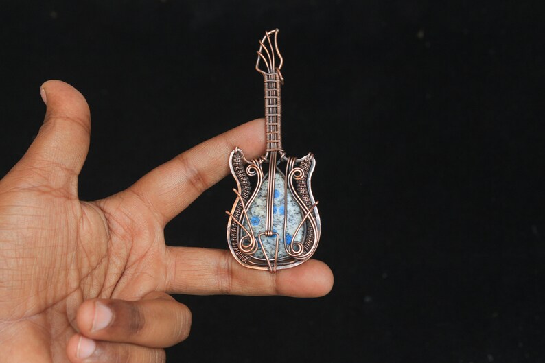 May include: A copper wire wrapped guitar pendant with a blue and white stone inlay.