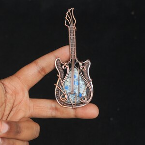 May include: A copper wire wrapped guitar pendant with a blue and white stone inlay.