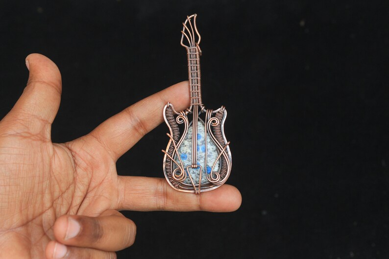 May include: A copper wire wrapped guitar pendant with a blue and white stone inlay.