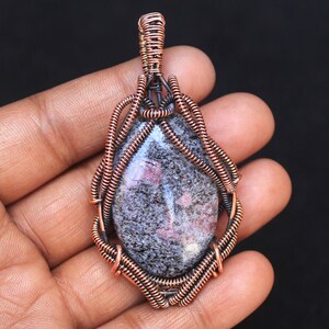 May include: A copper wire wrapped pendant featuring a grey and pink gemstone with a unique pattern.