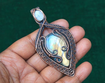 May include: A copper wire wrapped pendant featuring a large iridescent labradorite gemstone and a smaller white moonstone. The pendant is hand-crafted and has a unique, intricate design.