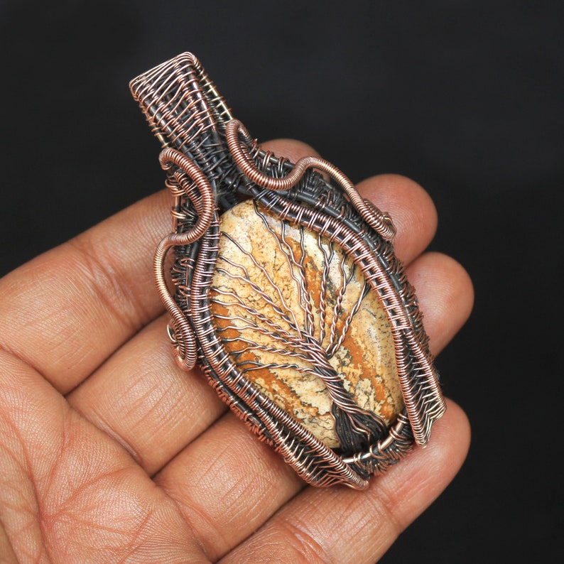 May include: A copper wire wrapped pendant featuring a tree agate stone with a brown, white, and orange pattern. The pendant is a unique piece of jewelry with a natural stone and wirework design.