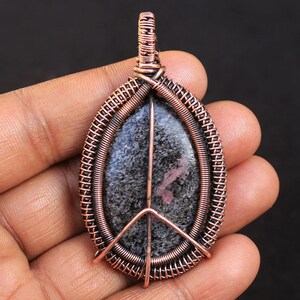 Op de afbeelding: Een hanger met koperdraad gewikkeld met een zwarte en roze edelsteen met een vredestekenontwerp.