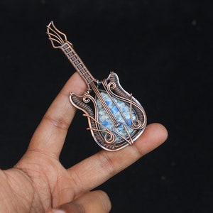 May include: A copper wire wrapped pendant shaped like a guitar with a blue and white stone in the center.