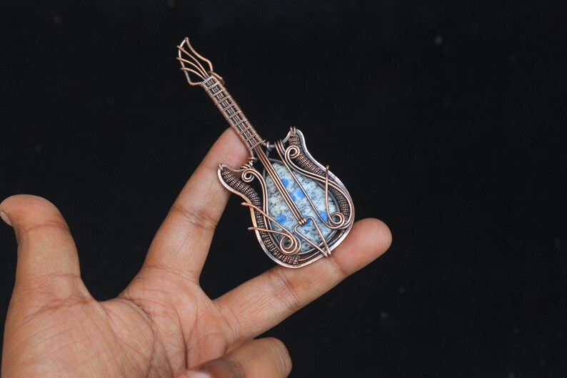 May include: A copper wire wrapped pendant shaped like a guitar with a blue and white stone in the center.