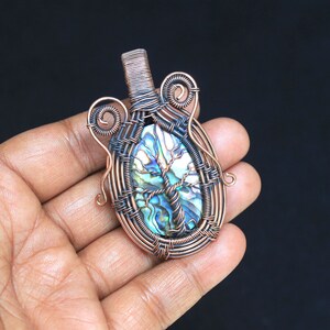 May include: A copper wire wrapped pendant featuring a blue, green, and iridescent abalone shell with a tree of life design.