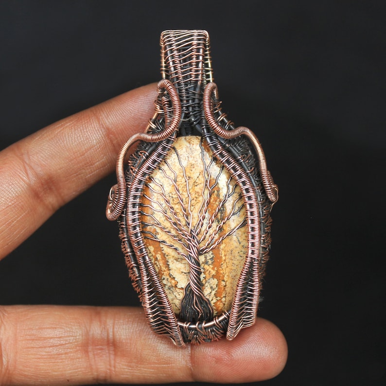 May include: A copper wire wrapped pendant featuring a tree agate stone with a natural tree pattern. The pendant is oval shaped and has a copper bail.