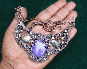 May include: A copper wire necklace with a purple and white stone and two green stones. The necklace is in the shape of a crescent moon and has a chain.