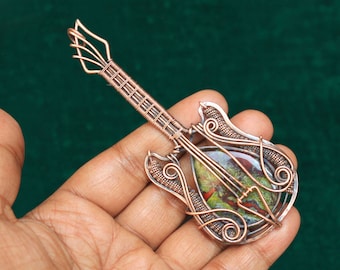 May include: A copper wire guitar pendant with a green and red agate stone in the center. The guitar is detailed with wirework and has a classic electric guitar shape.