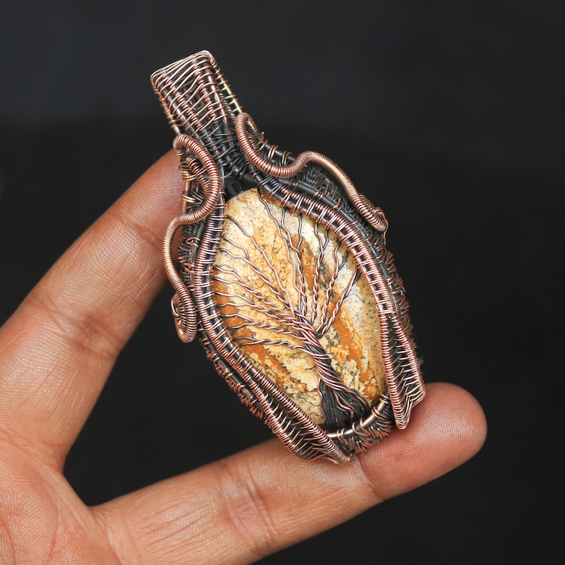 May include: A copper wire wrapped pendant featuring a tree of life design in a brown and beige stone.