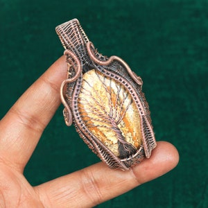 May include: A copper wire wrapped pendant featuring a tree of life design with a light brown and white agate stone.