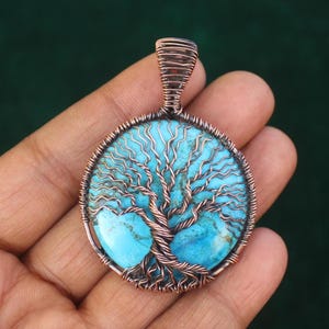 May include: A handcrafted pendant featuring a turquoise stone with a copper wire tree of life design. The pendant is round, with a copper wire bail for hanging. The turquoise stone has a light blue color.