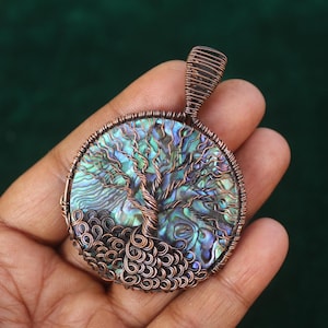 May include: A copper wire pendant with a tree of life design. The pendant's centre displays an iridescent abalone shell. The tree's branches and roots are intricately crafted with copper wire, creating a unique, nature-inspired accessory.