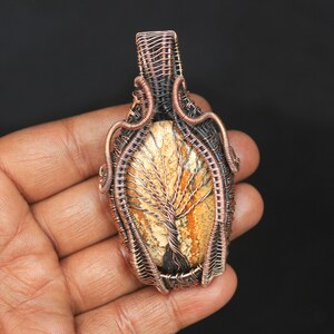 May include: A copper wire wrapped pendant featuring a tree agate stone with a natural tree pattern. The pendant is oval shaped and has a copper bail.