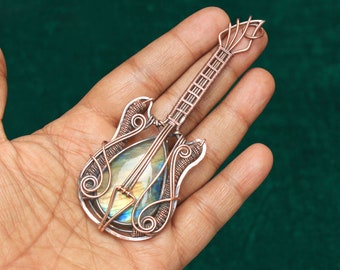 May include: A copper wire guitar pendant with a iridescent labradorite gemstone in the center. The guitar is intricately detailed with wirework and has a classic electric guitar shape.