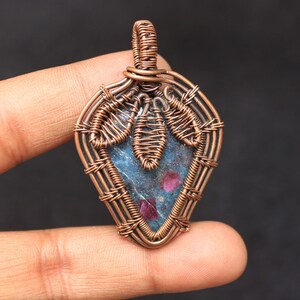 Puede incluir: Un colgante envuelto en alambre de cobre con una piedra preciosa azul y rosa y una anilla de cobre.