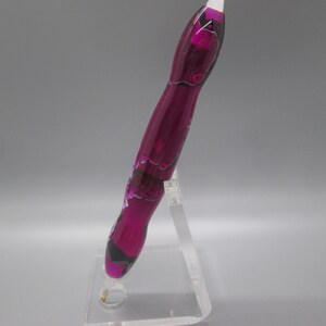 May include: A purple and black pen with a swirl design. The pen is on a clear acrylic stand.