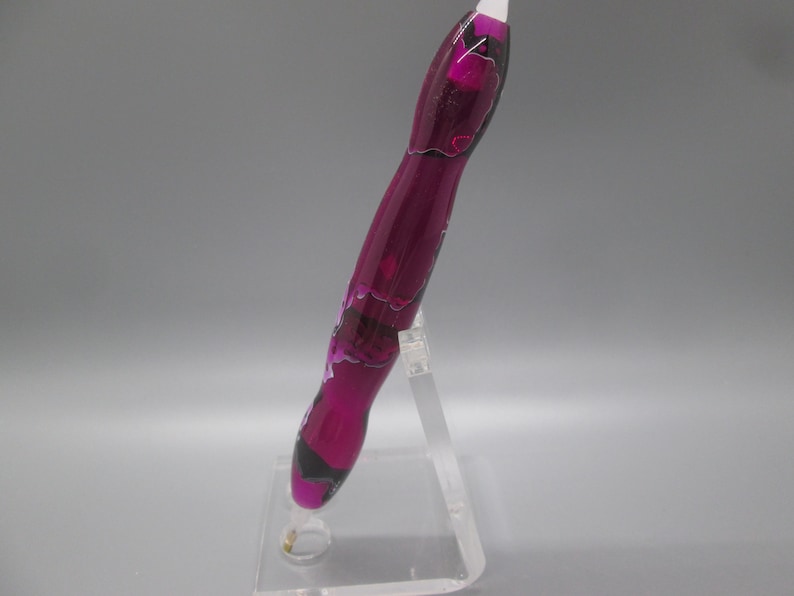 May include: A purple and black pen with a swirl design. The pen is on a clear acrylic stand.