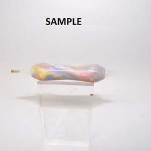 May include: A colorful, marbled, swirl pen with a gold tip. The pen is on a clear acrylic stand. SAMPLE is written in black text above the pen.