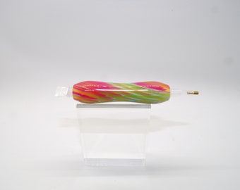 May include: A colorful diamond painting pen with a vibrant, swirled design. The pen features a combination of pink, yellow, and green hues. The pen is designed for detailed craft projects and is shown on a clear acrylic stand.