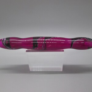 May include: A pink and black marbled pen with a clear tip. The pen is sitting on a clear acrylic stand.