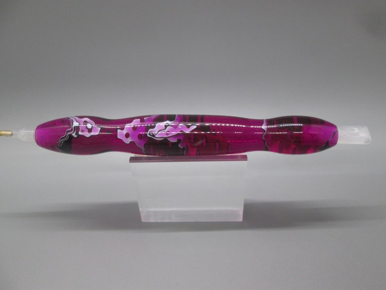 May include: A pink and black marbled pen with a clear tip and a gold metal tip.