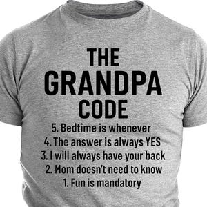 Może przedstawiać: Szara koszulka z napisem "THE GRANDPA CODE" w czarnym kolorze. Poniżej zasady: "5. Czas snu jest kiedykolwiek, 4. Odpowiedź zawsze brzmi TAK, 3. Zawsze będę cię wspierać, 2. Mama nie musi wiedzieć, 1. Zabawa jest obowiązkowa."