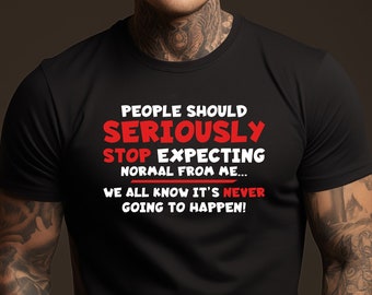 May include: Black crew neck t-shirt with the text "PEOPLE SHOULD SERIOUSLY STOP EXPECTING NORMAL FROM ME... WE ALL KNOW IT'S NEVER GOING TO HAPPEN!" in red and white. The shirt is worn by a person with tattoos.