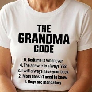 May include: A woman wearing a white t-shirt with the text "THE GRANDMA CODE" in bold black letters. The shirt also lists five rules, including "Hugs are mandatory" and "The answer is always YES."