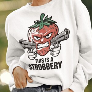 May include: White sweatshirt with a cartoon strawberry holding two guns and the text "This is a Strobbbery".
