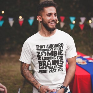 May include: White t-shirt with black text that reads "That awkward moment when a zombie is looking for brains and it walks right past you".