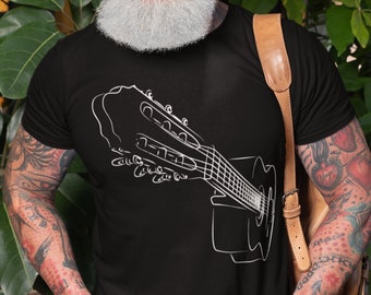 May include: A man wearing a black t-shirt with a white outline of a guitar on the front. He is smiling and has a white beard and gray hair. He is wearing a brown leather strap over his shoulder.
