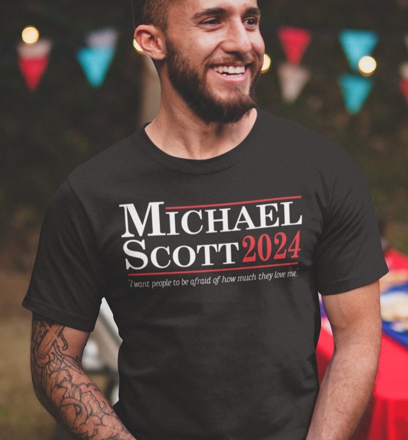 May include: Black t-shirt with white text that reads "MICHAEL SCOTT 2024" and the smaller text "I want people to be afraid of how much they love me."