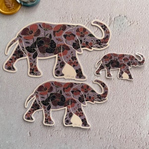 K&ouml;nnte beinhalten: Drei Elefanten-Aufkleber mit floralem Muster. Der gr&ouml;&szlig;te Elefant ist lila und hat ein dunkles Blumenmuster. Der mittlere Elefant ist lila und hat ein dunkles Blumenmuster. Der kleinste Elefant ist lila und hat ein dunkles Blumenmuster.
