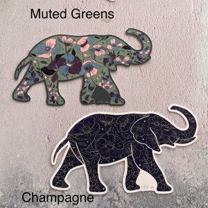 K&ouml;nnte beinhalten: Zwei Elefanten-Silhouetten-Aufkleber mit Blumenmustern. Der obere Aufkleber ist mattgr&uuml;n mit rosa und violetten Blumen. Der untere Aufkleber ist schwarz mit goldenen Blumen. Der Text "Muted Greens" befindet sich &uuml;ber dem oberen Aufkleber und "Champagne" unter dem unteren Aufkleber.