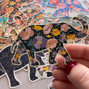 K&ouml;nnte beinhalten: Ein schwarzer Elefanten-Aufkleber mit einem floralen Muster in Rosa-, Lila-, Gelb- und Wei&szlig;t&ouml;nen. Der Elefant steht auf allen vieren mit erhobenem R&uuml;ssel.