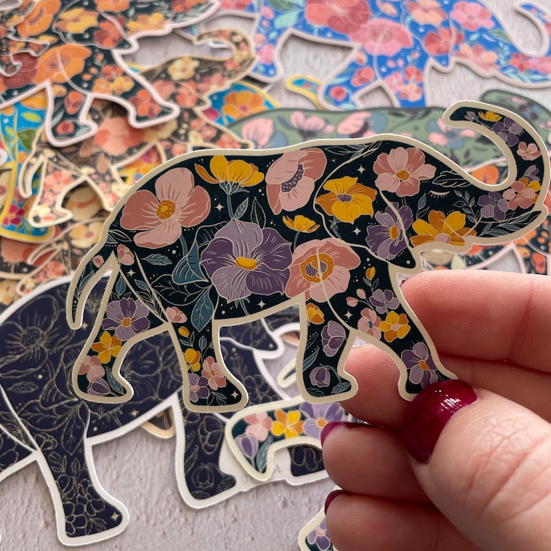 K&ouml;nnte beinhalten: Ein schwarzer Elefanten-Aufkleber mit einem floralen Muster in Rosa-, Lila-, Gelb- und Wei&szlig;t&ouml;nen. Der Elefant steht auf allen vieren mit erhobenem R&uuml;ssel.