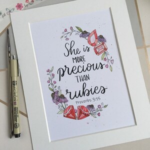 May include: A watercolour illustration of a floral wreath with red gemstones and the text "She is more precious than rubies Proverbs 3:15".
