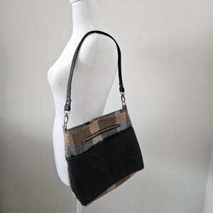 Bolso de hombro a cuadros en color camello gris y negro con correa de cuero y herrajes de latón antiguo. Tiene un bolsillo interior y tres bolsillos exteriores.