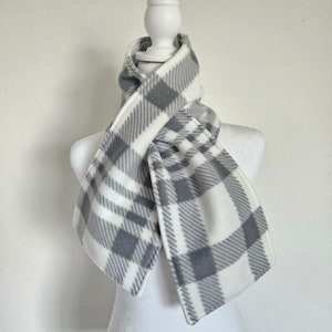 May include: A white and gray plaid fleece scarf. The scarf is folded and tied around a white mannequin's neck.